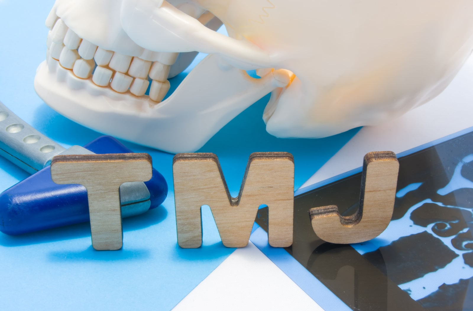 Three wooden blocks sitting up next to each other, and they spell out "TMJ" which stands for temporomandibular joint disorder