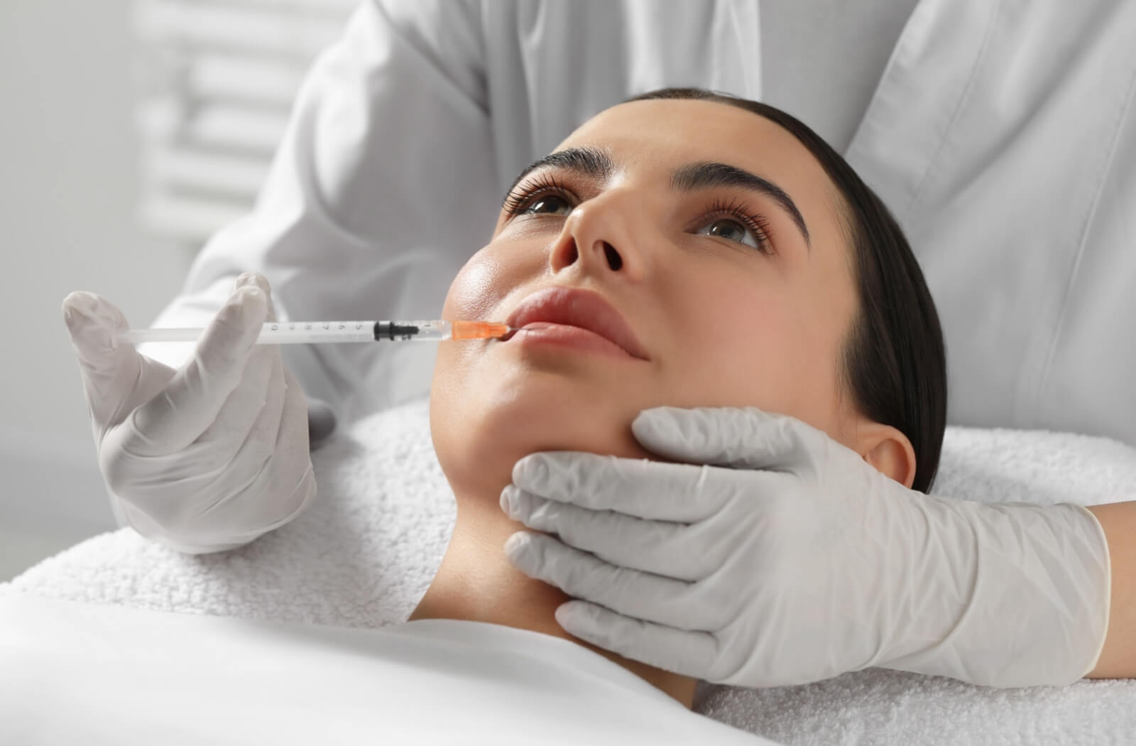 A woman receiving a lip filler injection in a clinic.