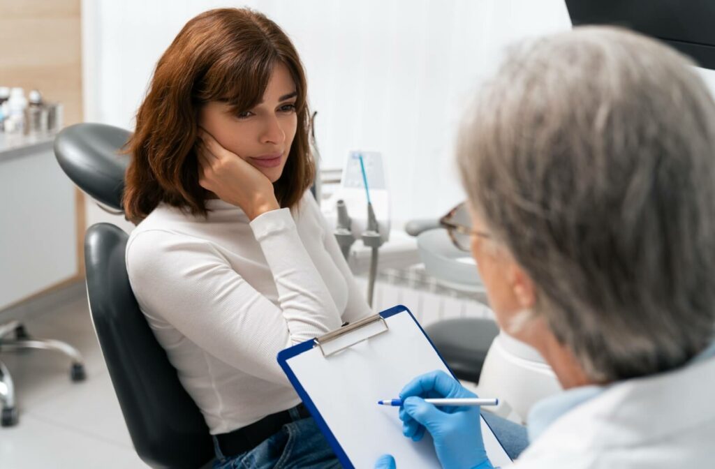 A woman rubbing her jaw in discomfort while talking to her dentist to learn if Botox can help her TMJ.