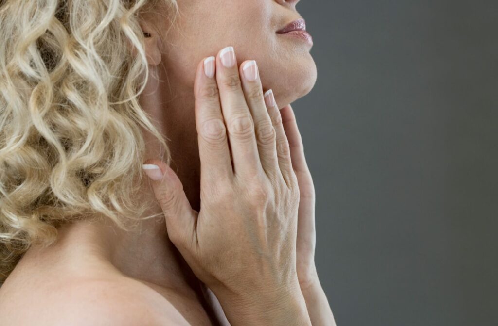 Close-up of the bottom half of a person's face as they touch their jawline looking for jowls.