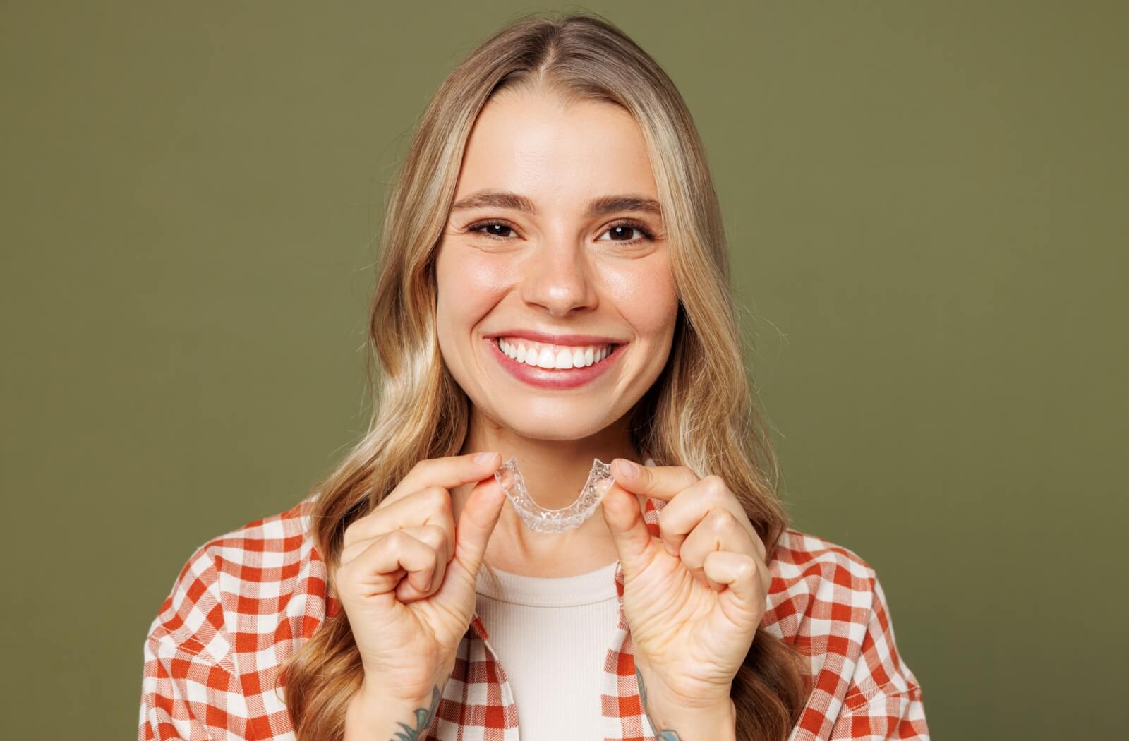 A happy adult with a healthy smile holding a transparent Invisalign aligner in both hands.