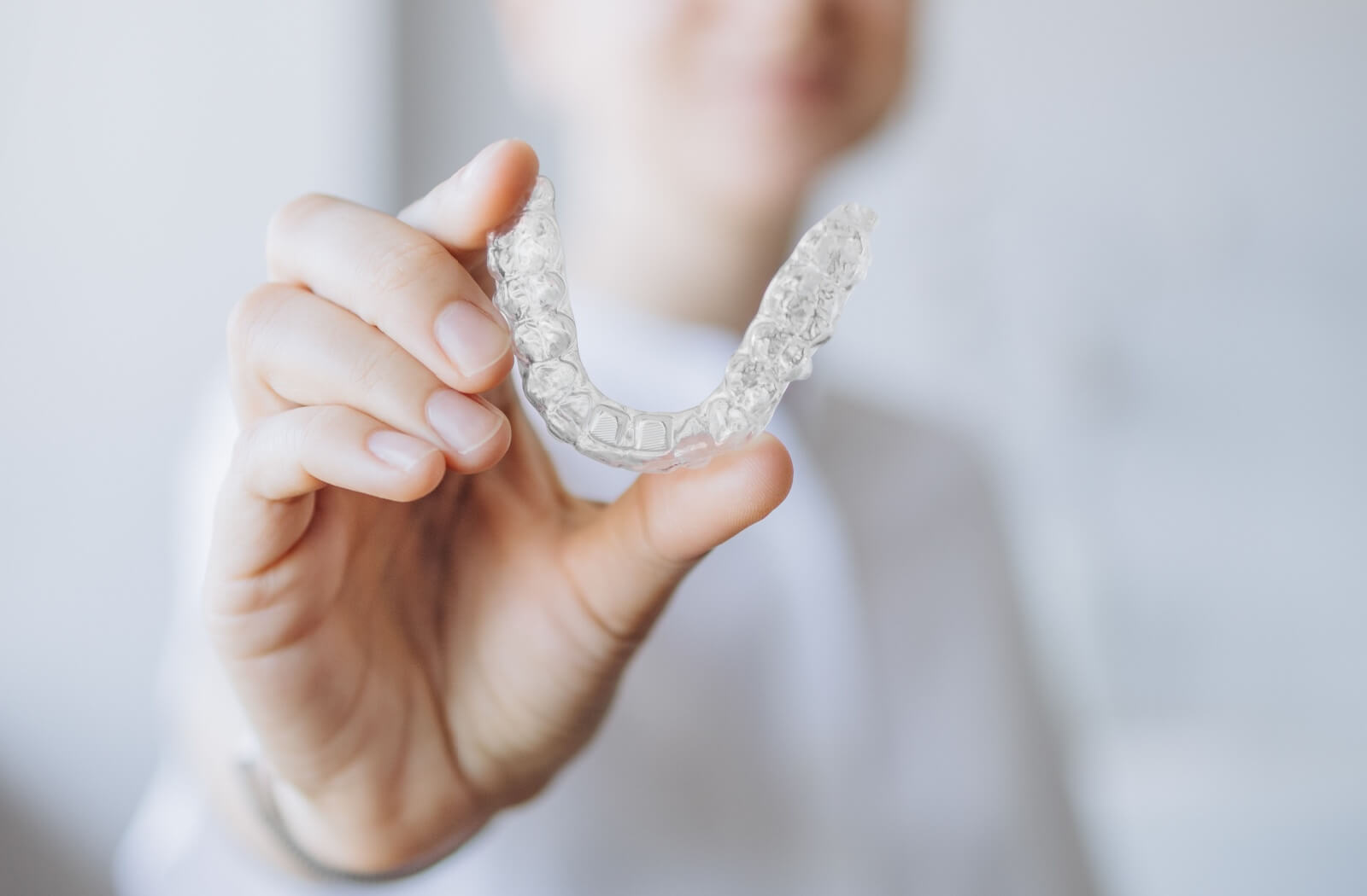 A close-up image of someone holding up a clear aligner.