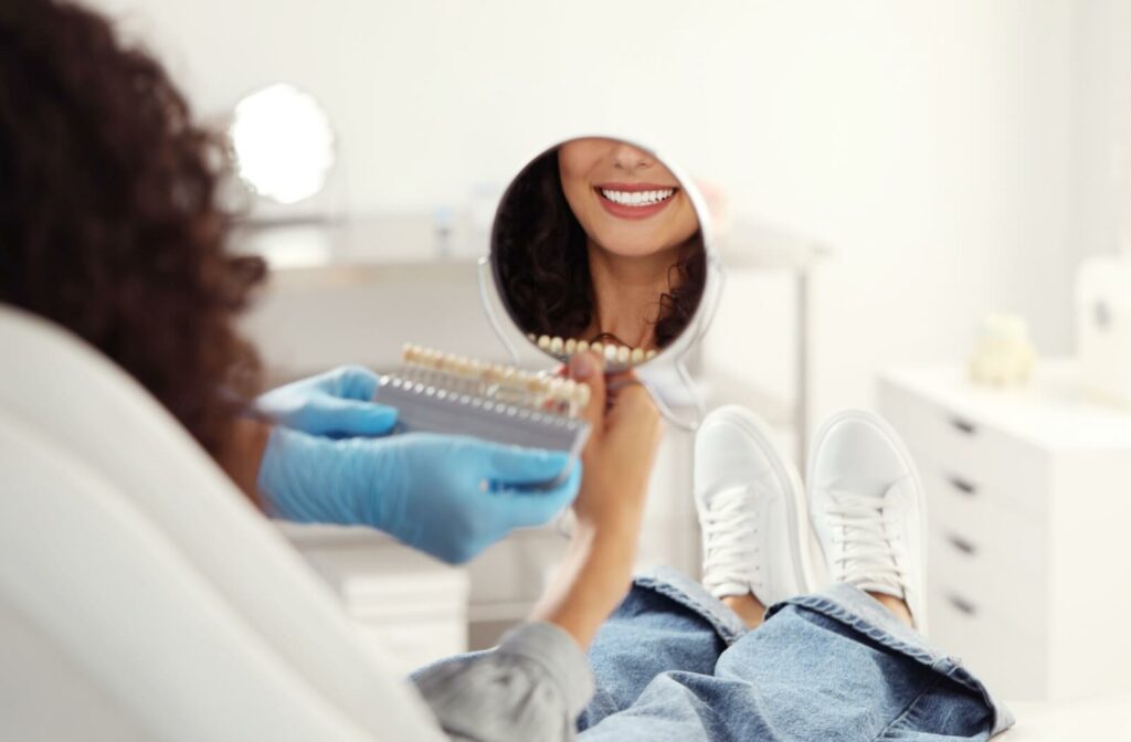 A person sitting in an esthetician's chair looking at their teeth in a handheld mirror