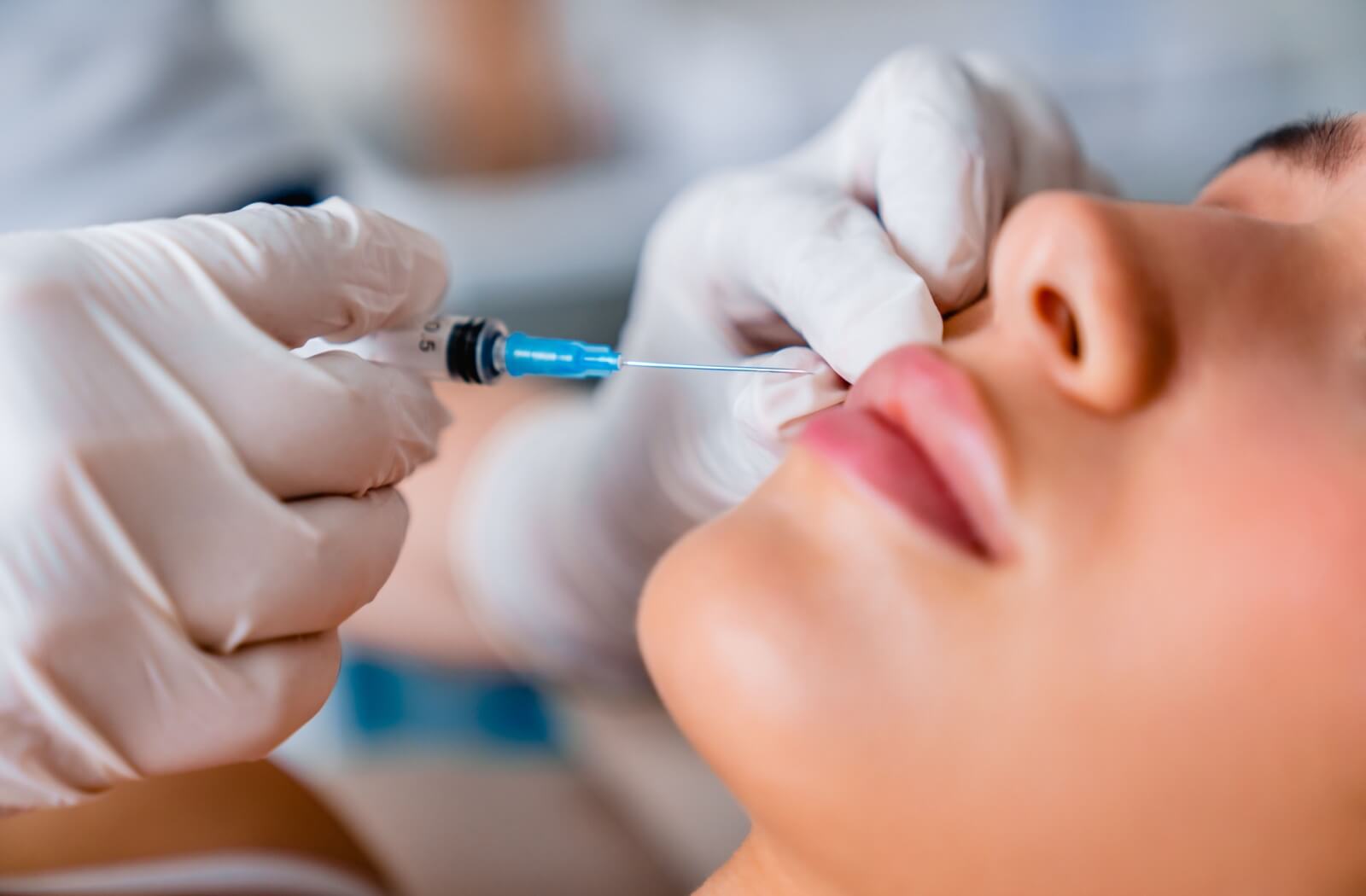 Close-up of a woman receiving a lip filler injection from a medical professional wearing gloves.