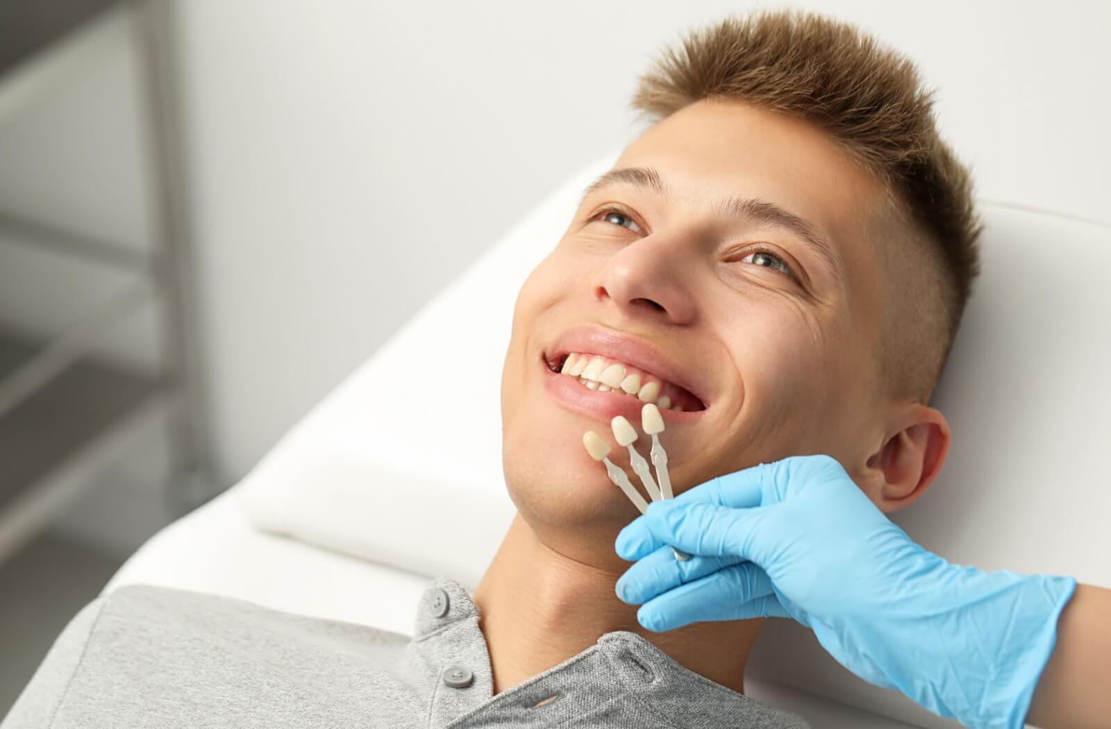 A dental professional using a shade guide to match a new dental crown to a smiling patient's natural teeth.